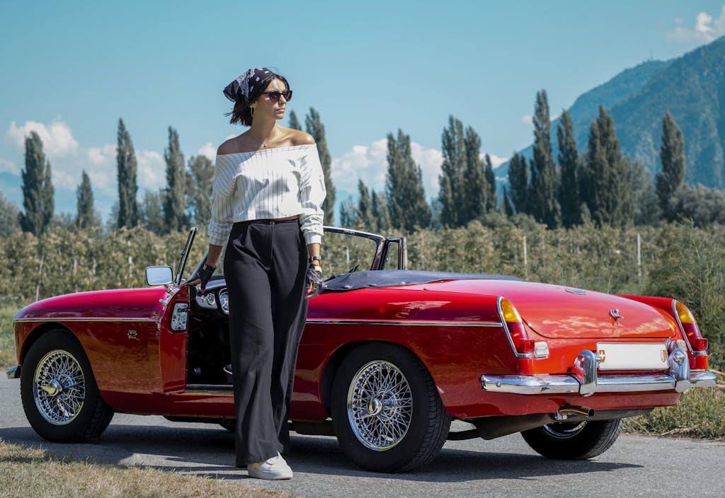 Fashionable woman standing by a classic red convertible car outdoors in Saxon.